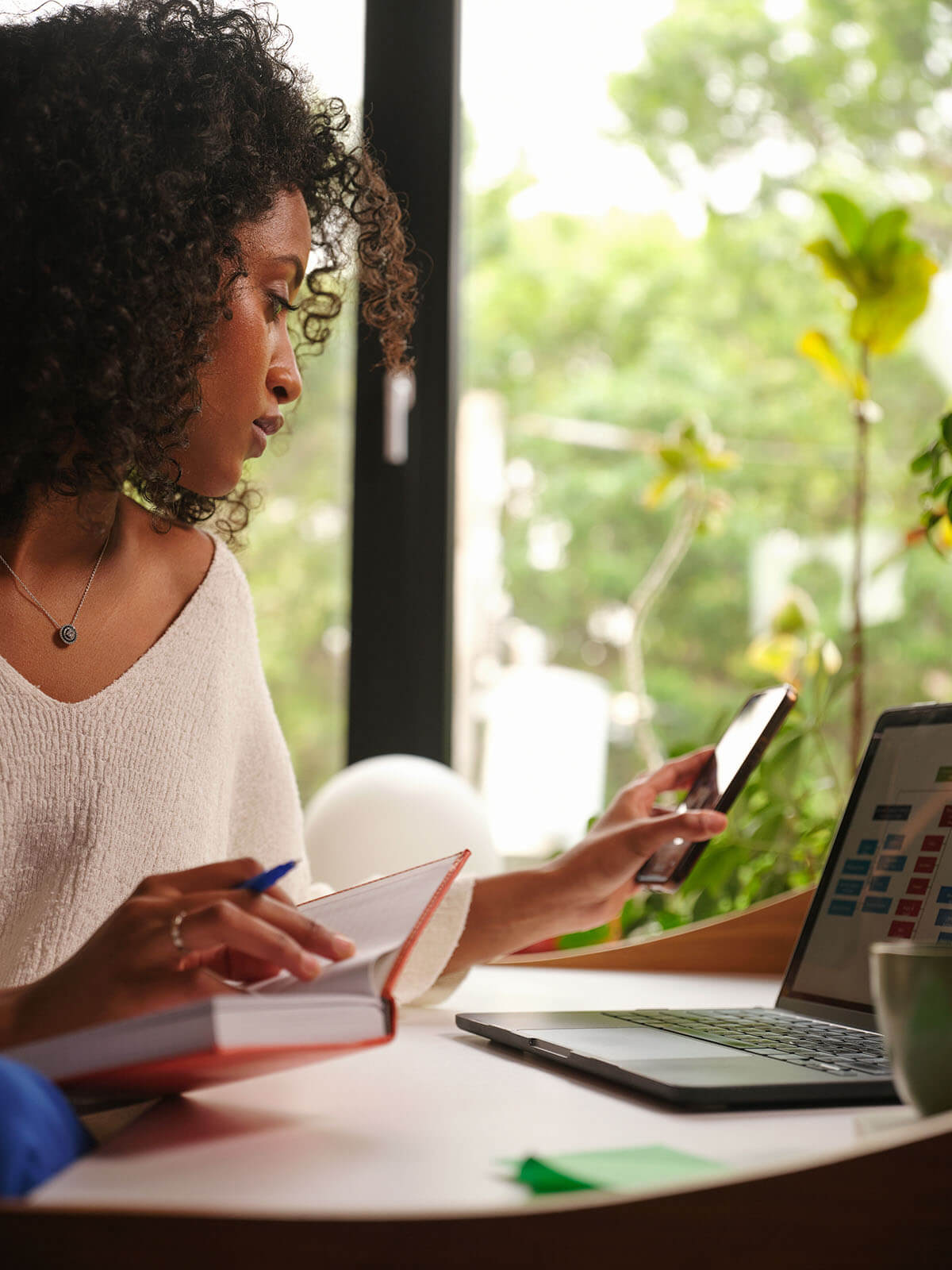 Intégration à distance : femme travaillant à domicile, consultant son téléphone et son agenda tout en configurant un plan d'intégration sur son ordinateur